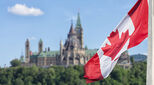 Canadian flag waving with Parliament Buildings hill and Library