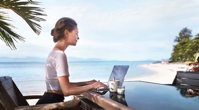 young millennial working on laptop on a beach