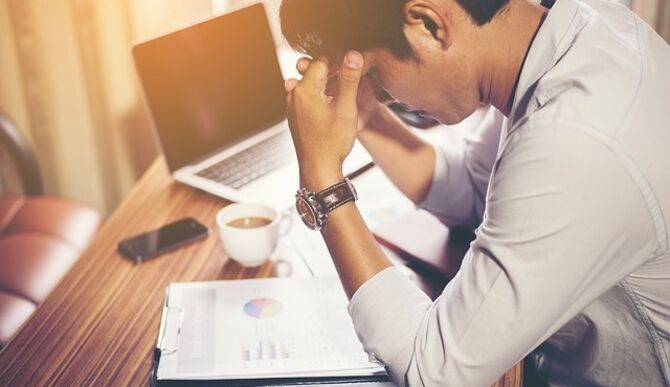 Image of man at desk holding head in hands